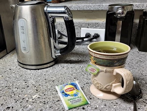 Electric tea pot with a prepared cup of tea on a counter