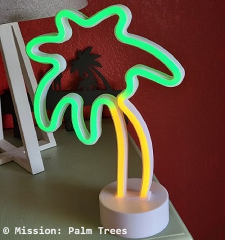 Fake neon palm tree lit up, sitting a a table.