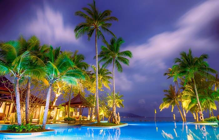 Asian resort with nighttime palms around a pool