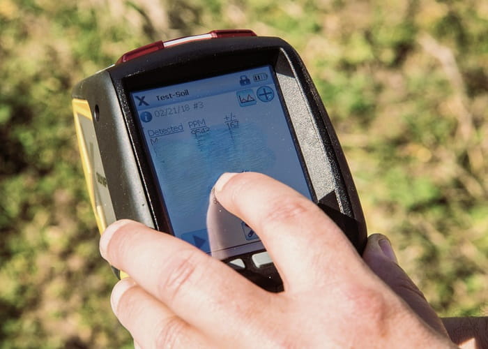 person with their hand on a meter that reads soil conditions