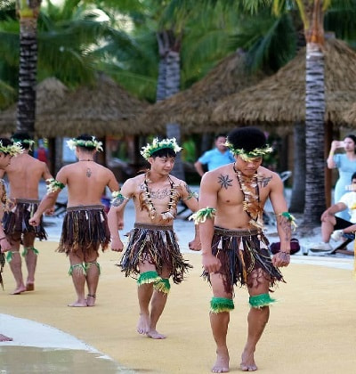 men performing a cultural dance wearing skirts of palm fronds