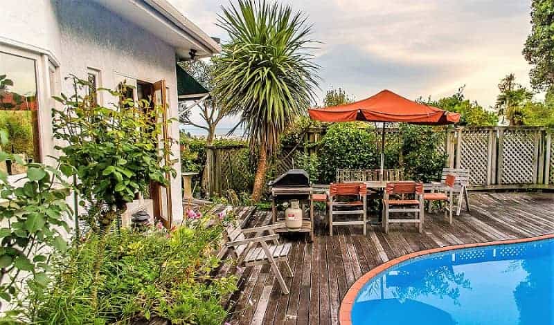 A palm-like tree placed in one corner of your backyard is a fabulous focal point. Deck around a pool with wooden fence, plants and a palm-like tree