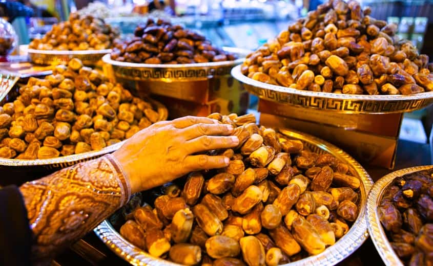 woman's hand choosing dates from a bowl surrounded by more bowls with other date varieties.