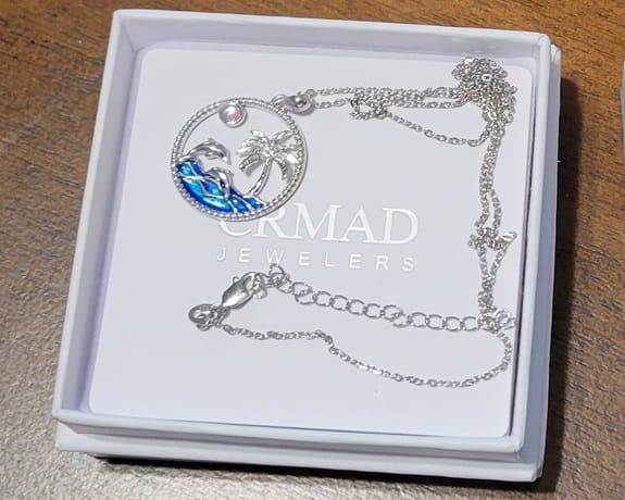 necklace opened from its box, with palm trees, blue ocean and dolphin